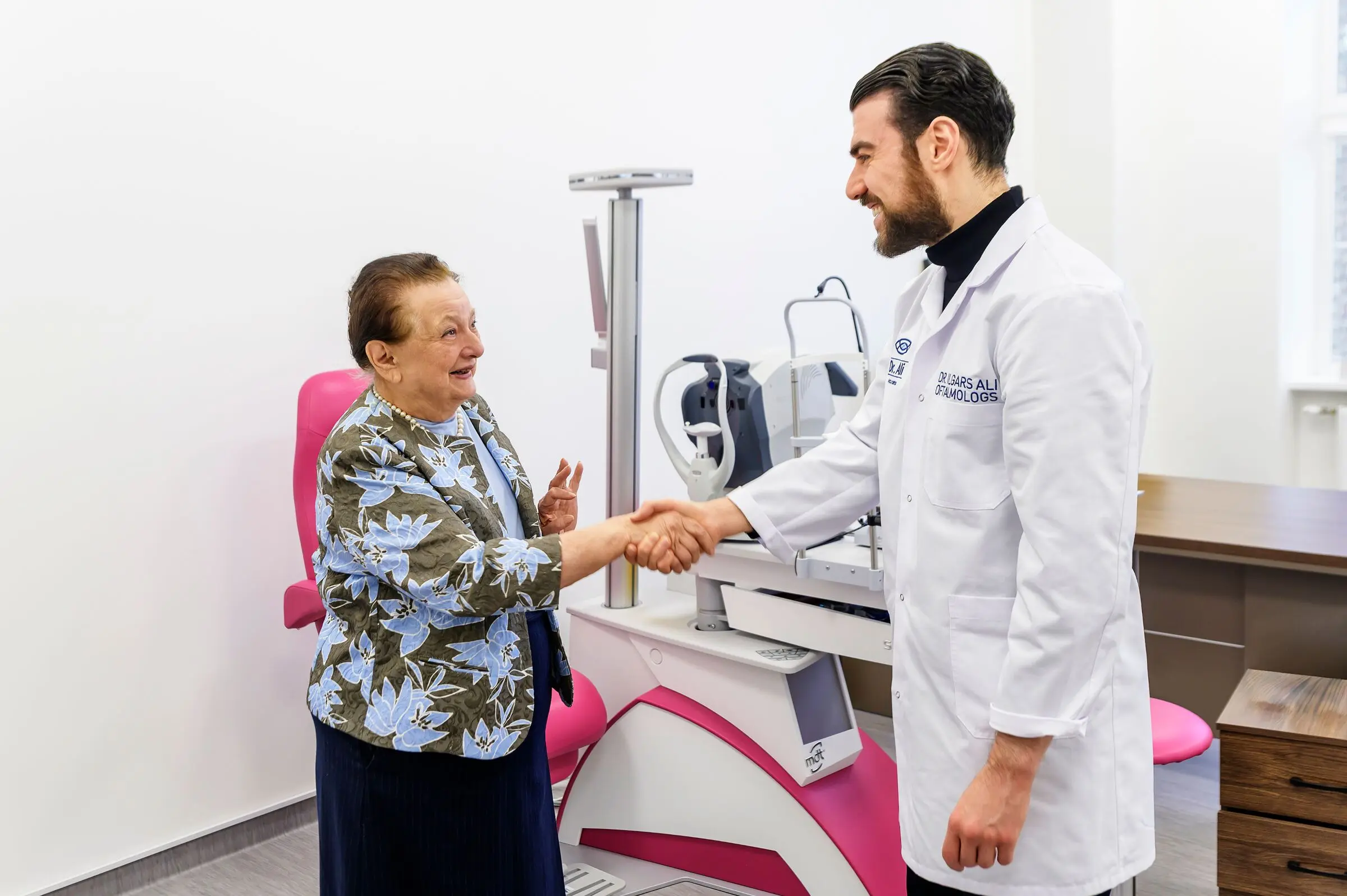 Dr. Ali sasveicinās ar pacienti izmeklējumu kabinetā